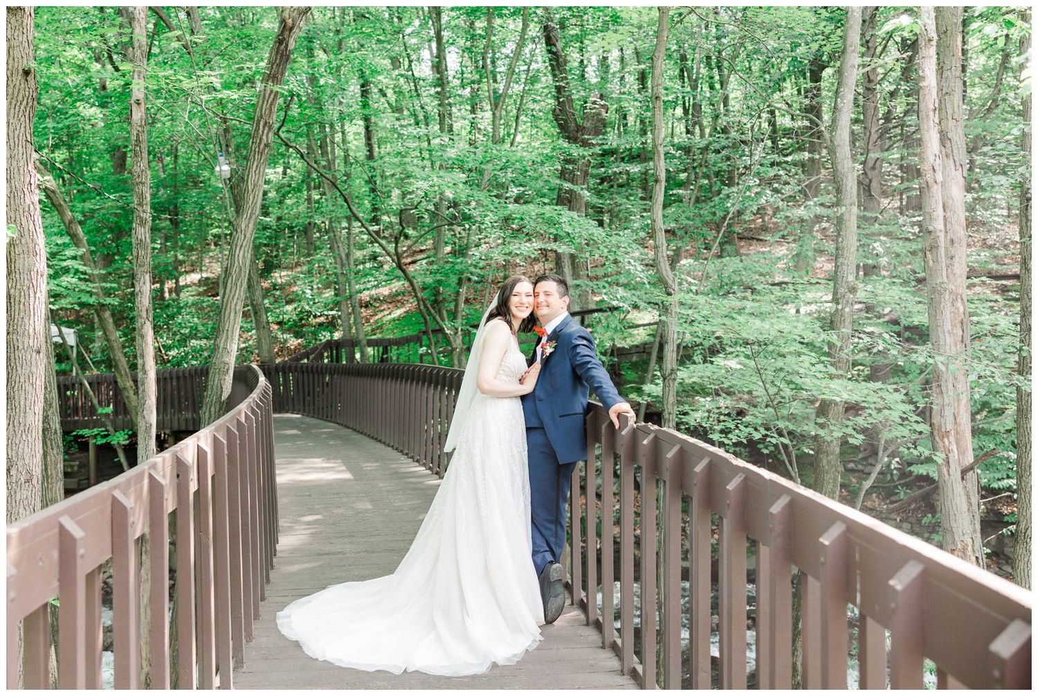 Bride and groom share an intimate moment on a wooden bridge surrounded by dense green forest.