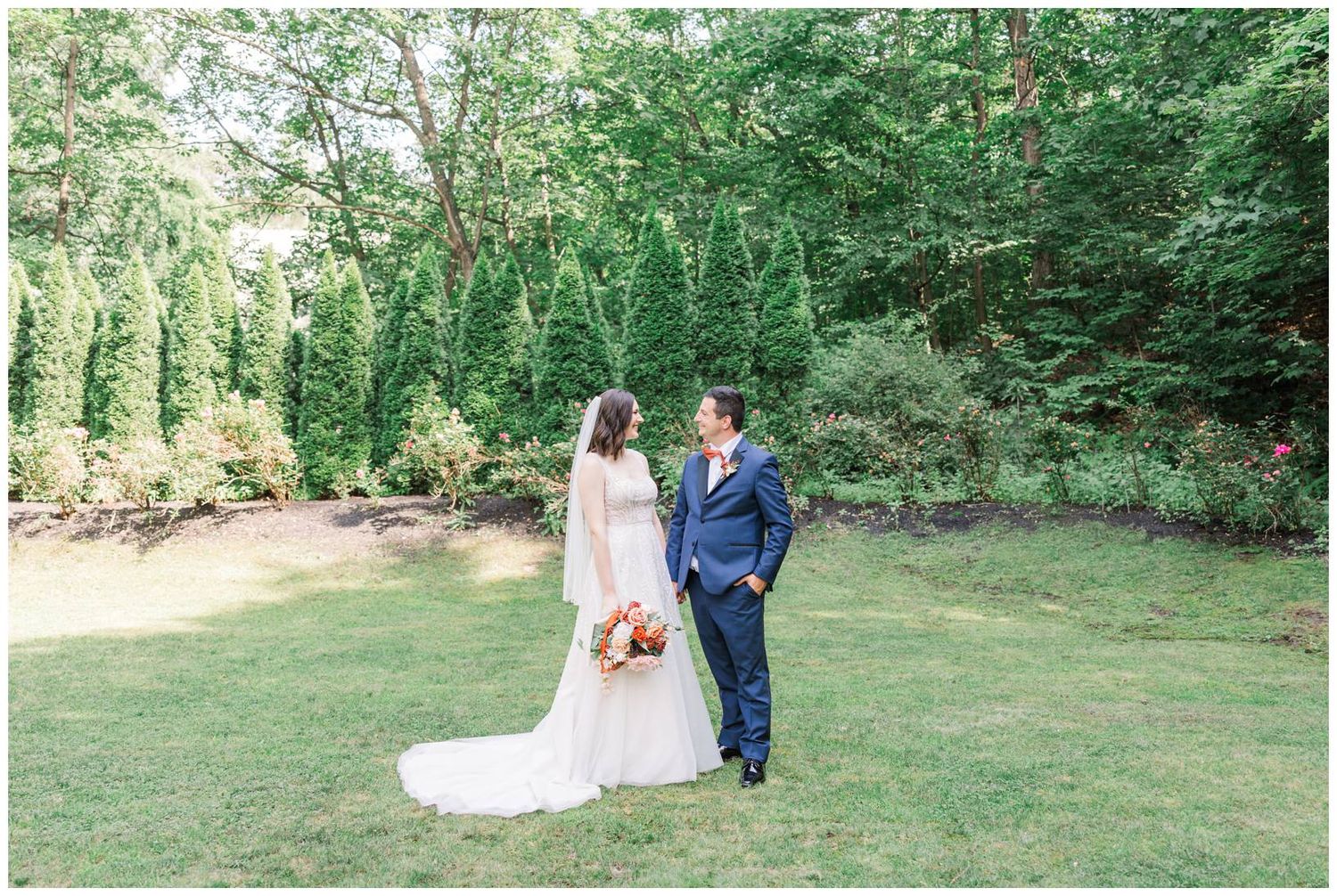 Wedding couple poses for portraits on an expansive lawn surrounded by natural greenery.