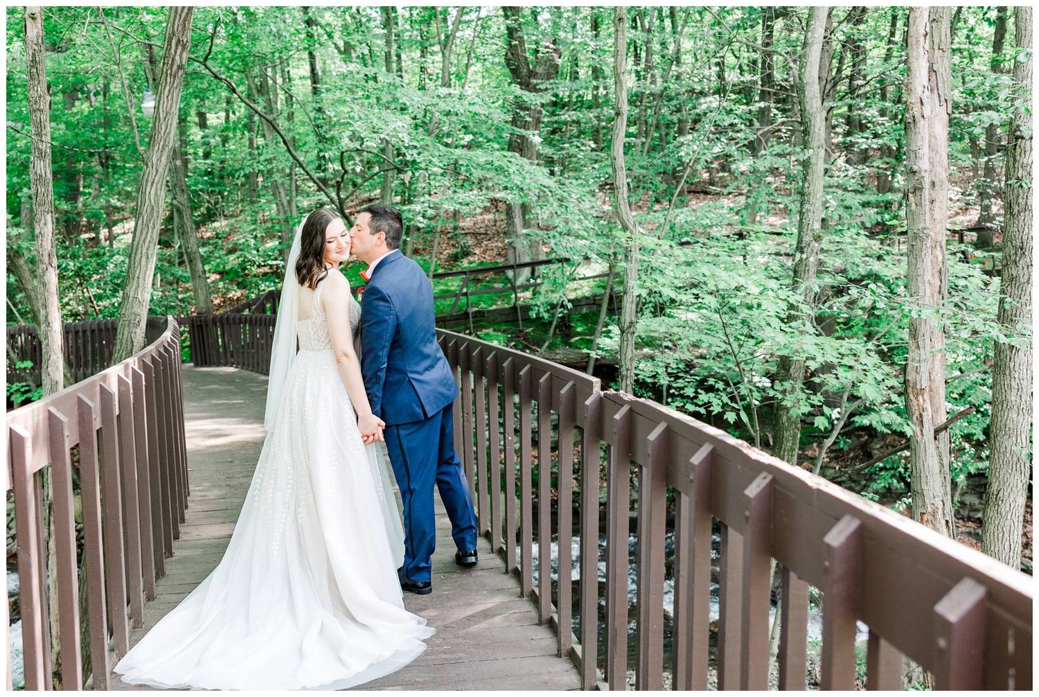 Couple sharing a romantic moment on a wooden bridge surrounded by lush forest greenery.