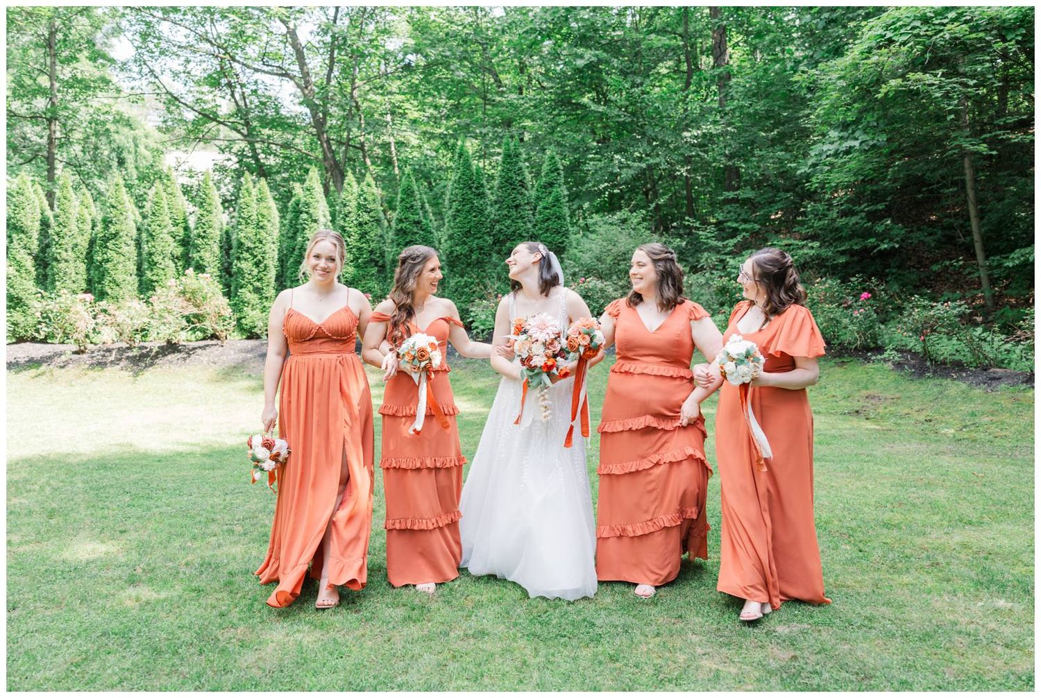 Wedding party poses outdoors with bridesmaids in vibrant coral dresses alongside the bride in white.
