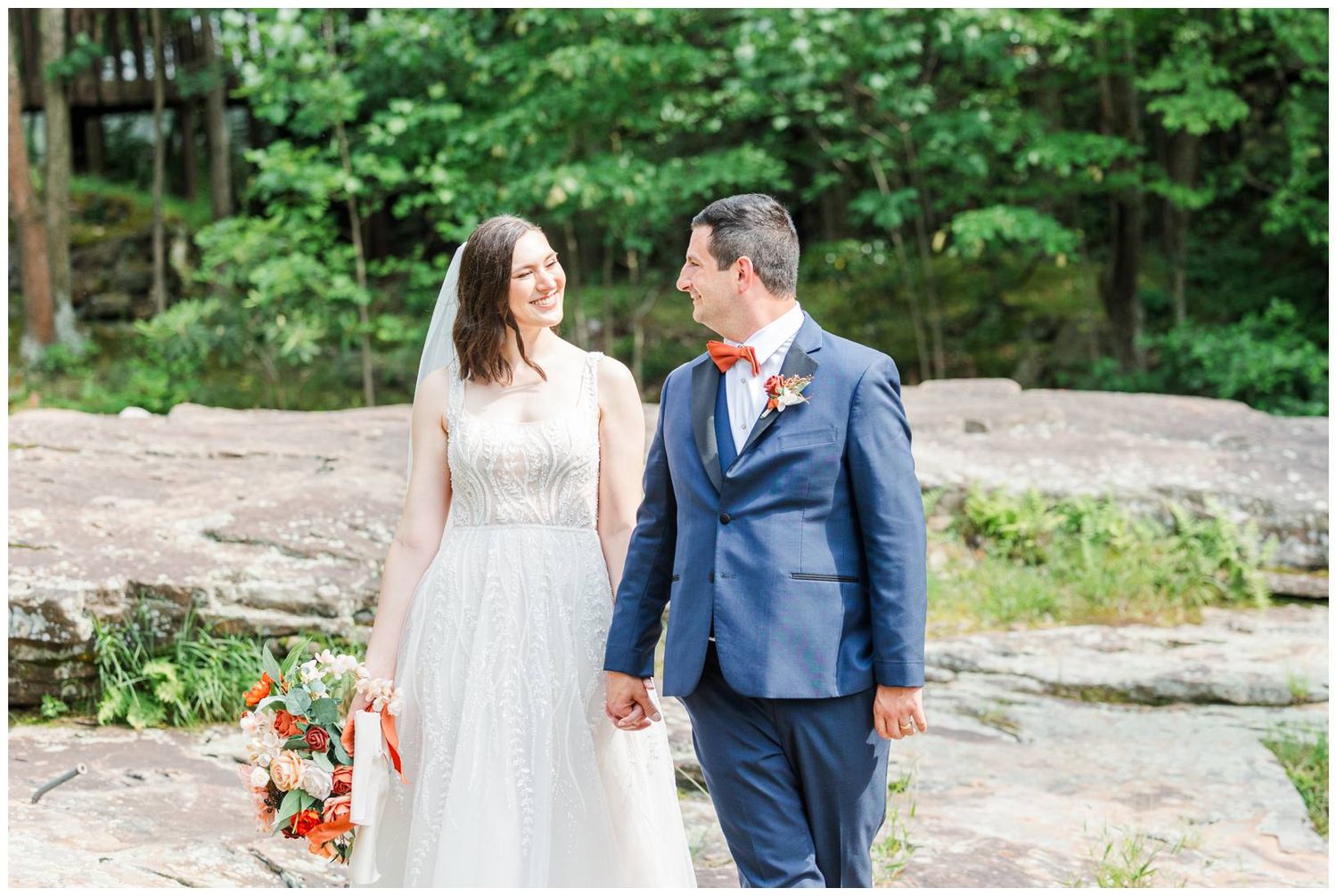 Wedding couple walking hand in hand through lush green forest setting.
