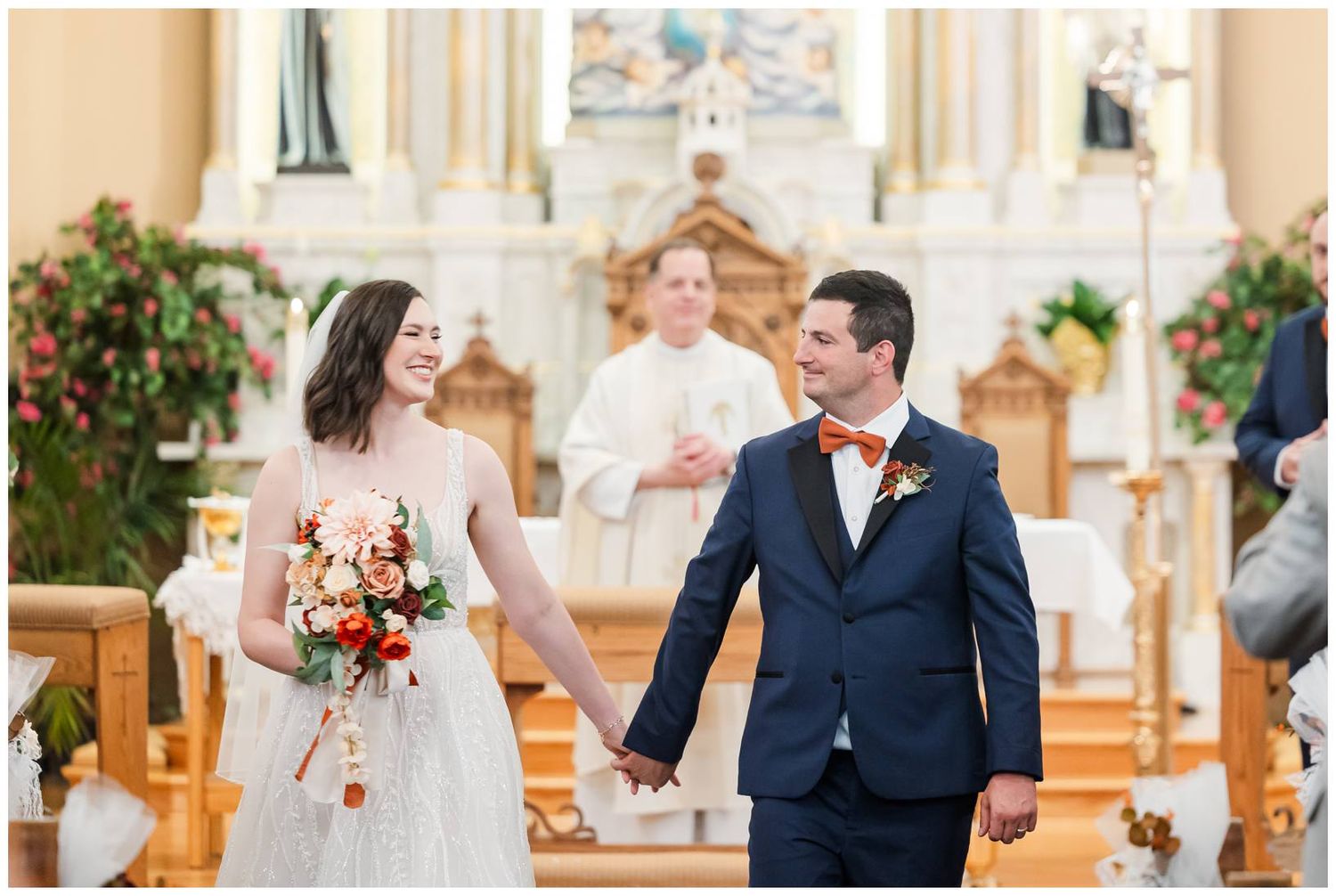 Wedding couple exchanging vows at beautiful Catholic church altar with religious statues and candles.