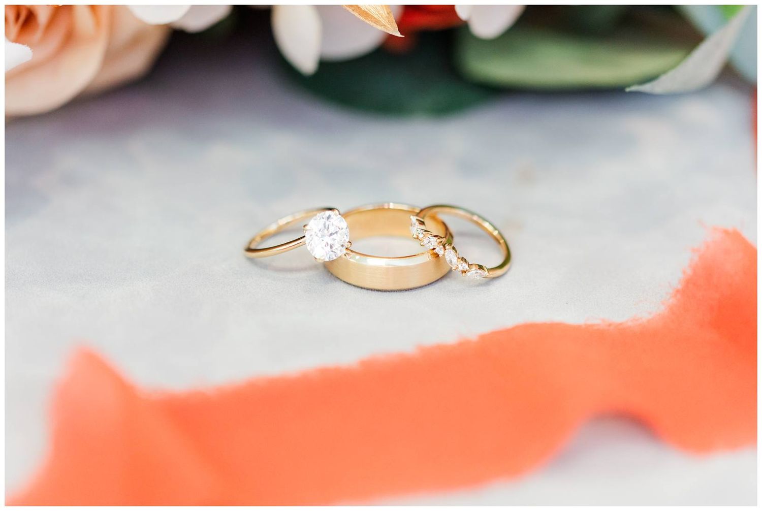 Three delicate wedding rings arranged artistically on a coral-colored surface.
