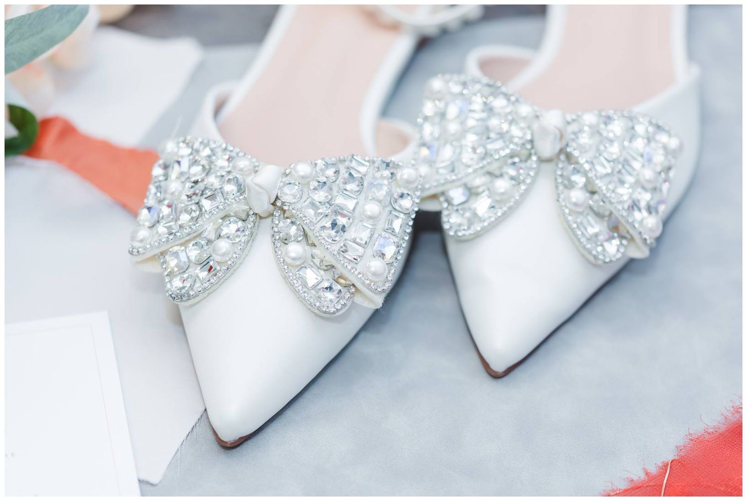 Elegant white bridal shoes adorned with sparkly crystal bow clips on the toes.