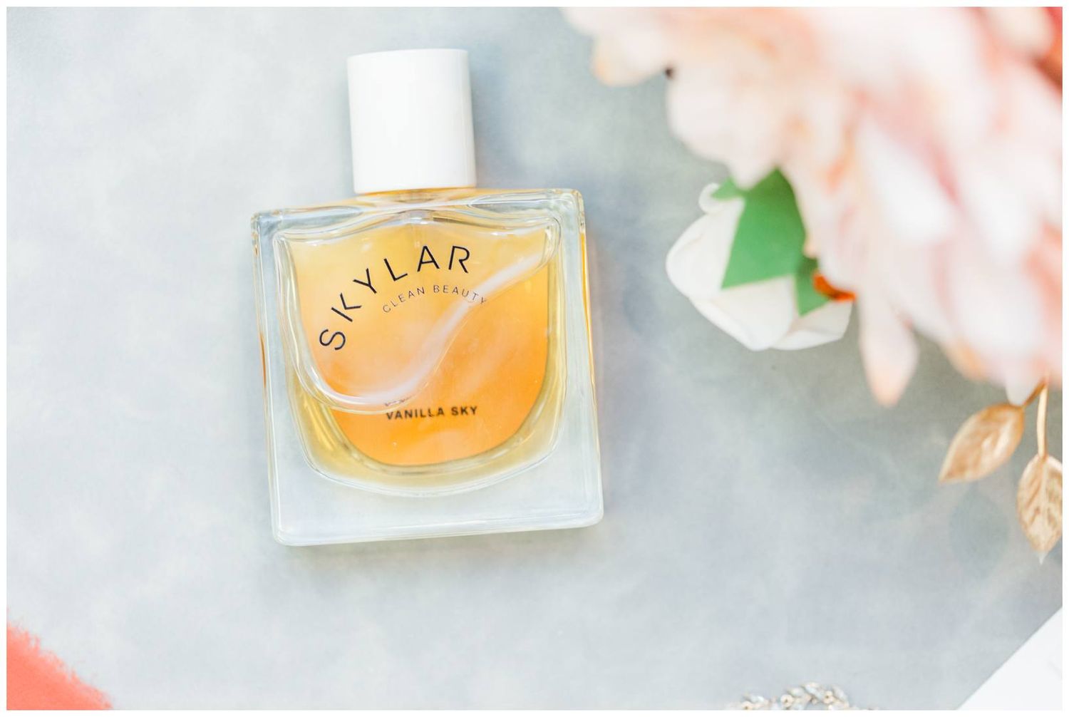 Bottle of Skylar perfume with orange and pink tones photographed against a soft background with floral elements.