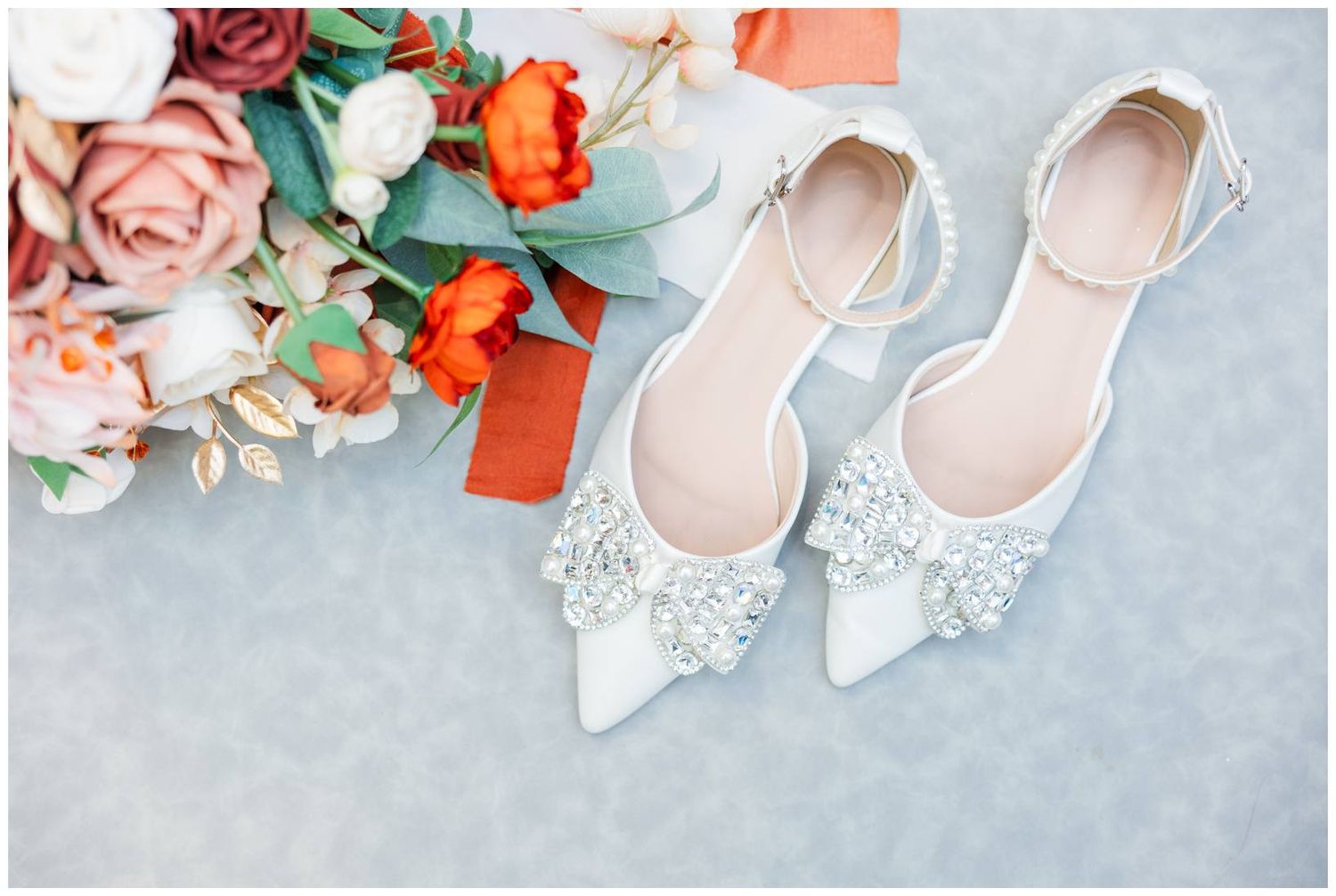Elegant bridal shoes with delicate lace detailing surrounded by pink and orange floral arrangements.