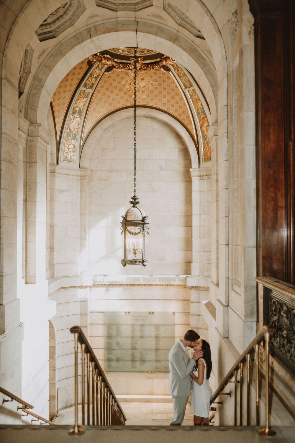 Intimate moment captured under ornate arched ceiling with hanging lanterns in marble hallway.