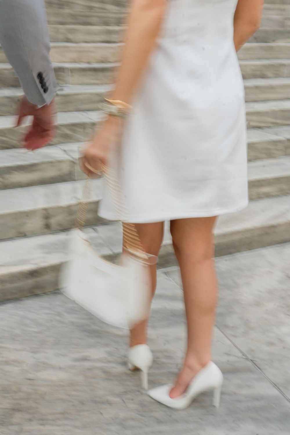 Motion blur captures movement on marble steps showing white dress and heels.