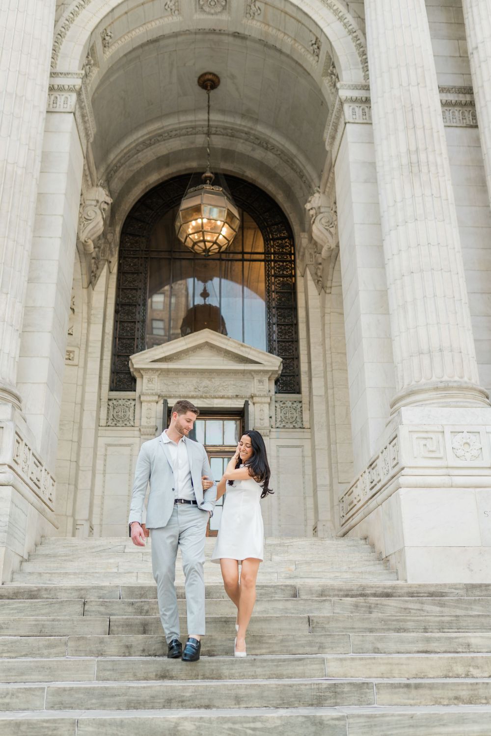 Elegant couple poses on grand marble steps of historic building with classical architecture.