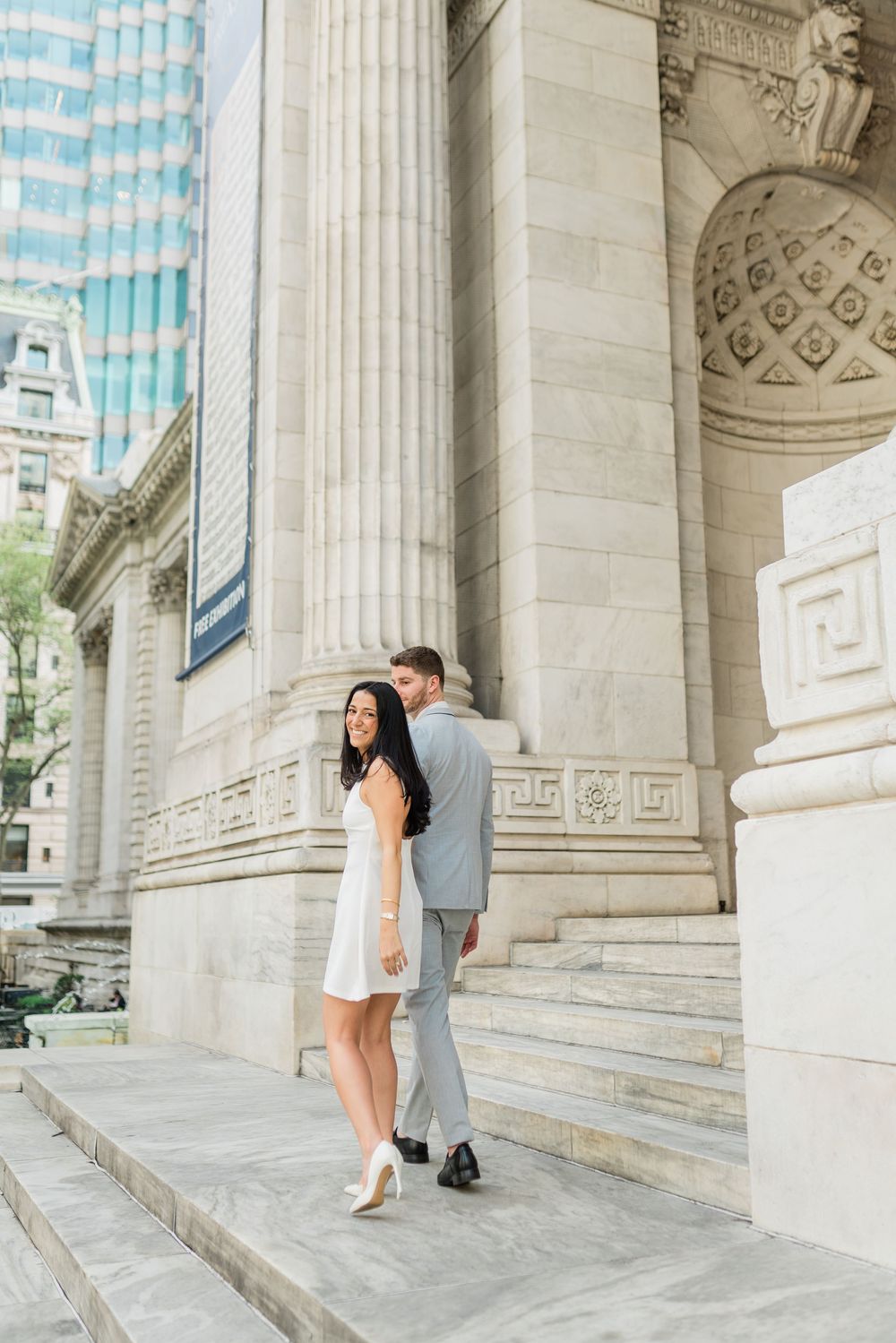 Engagement photos against backdrop of classical architecture with blue sky peeking through.