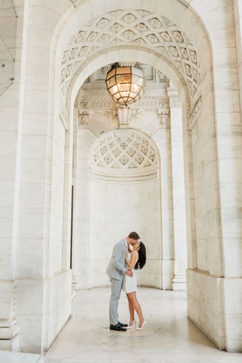 Romantic moment captured under ornate arched marble hallway with detailed ceiling patterns.
