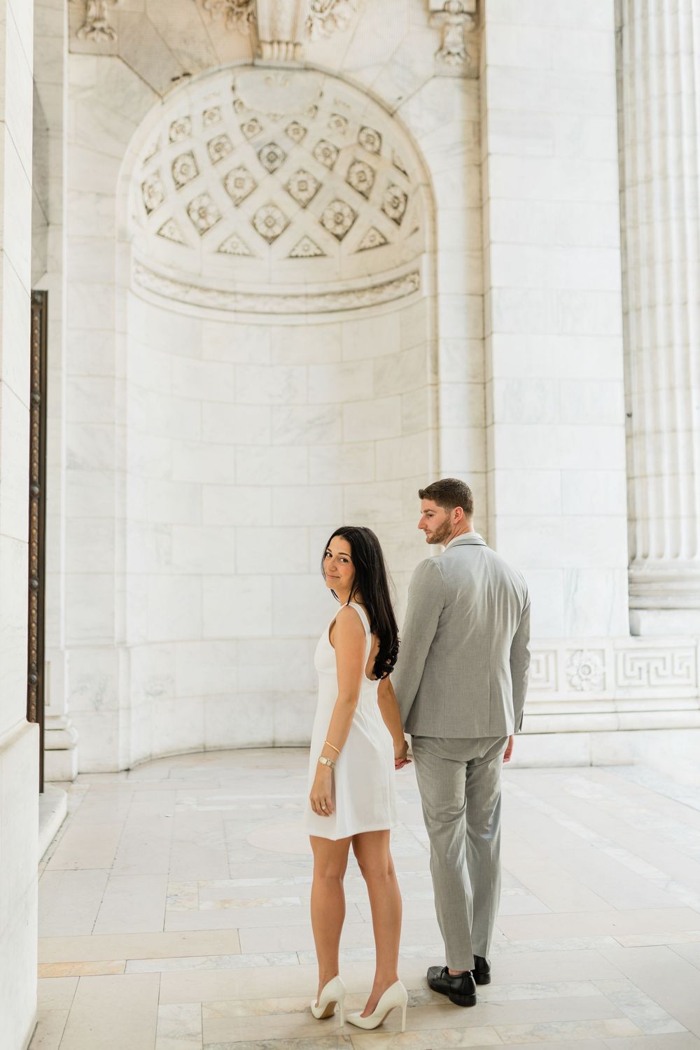 A stylish couple stands beneath ornate classical architecture with detailed dome ceiling.