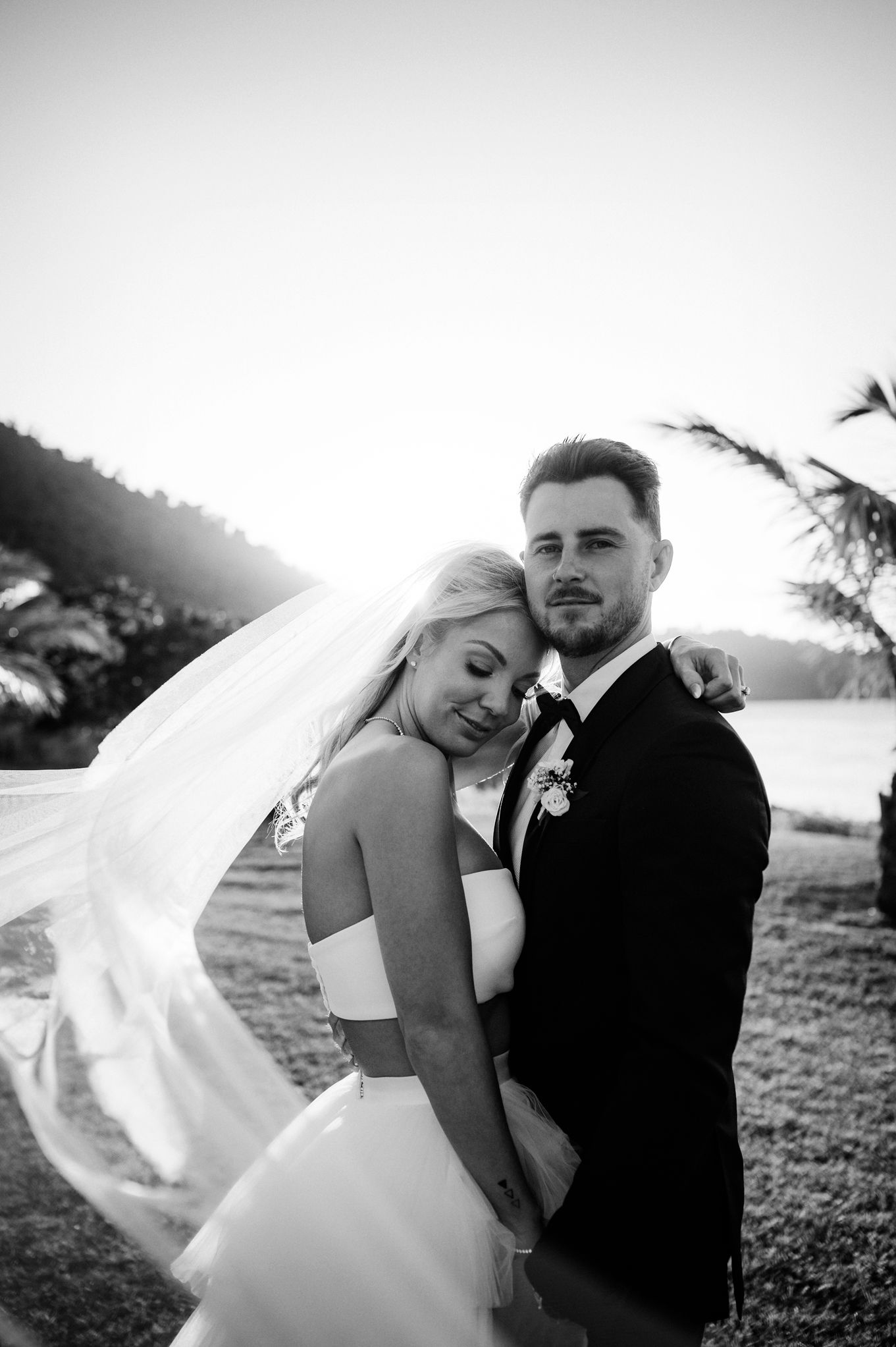 Black and white wedding portrait capturing a romantic seaside moment at golden hour.