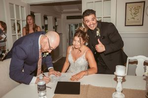 Wedding couple and guests gather around a table to sign documents during the ceremony.
