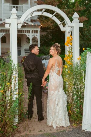 A couple stands under a white garden arbor with yellow flowers and greenery on their wedding day.