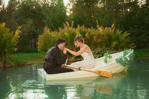 Newlyweds sharing romantic moment in small white boat on tranquil pond at sunset.