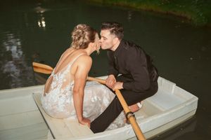 A couple shares a romantic kiss while sitting in a small rowboat on a dark lake at night time.