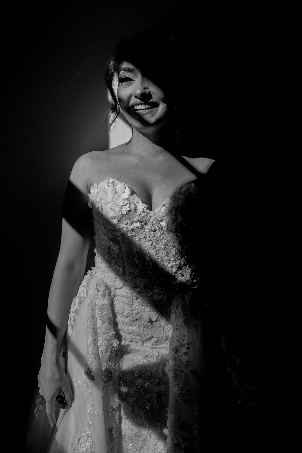A black and white artistic series showing close-up details of an elegant lace wedding dress against a dark background.