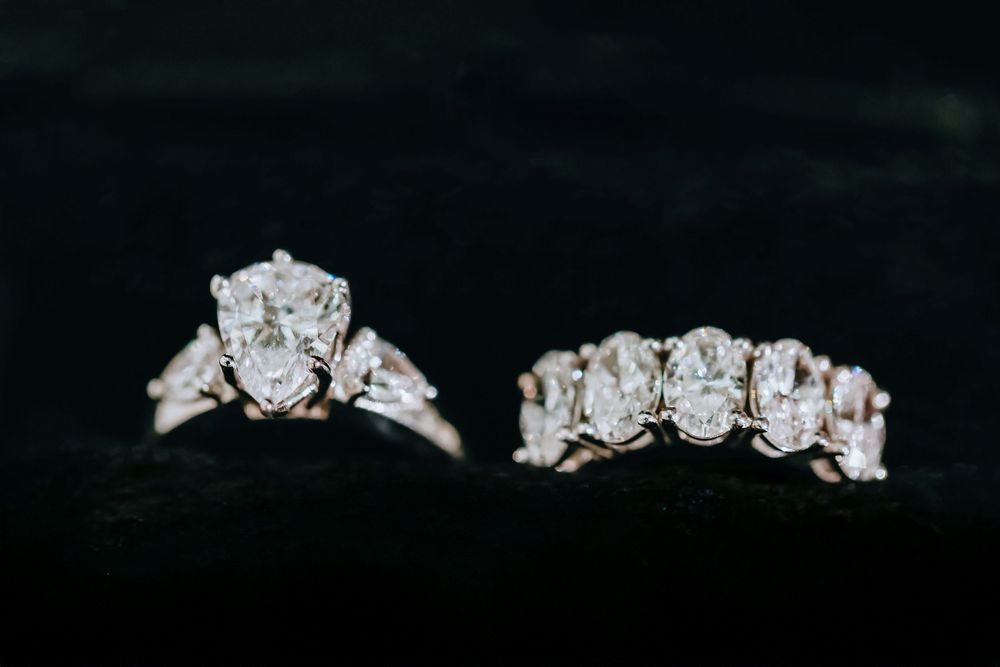 Two sparkling diamond rings with oval cut center stones displayed on a black background.