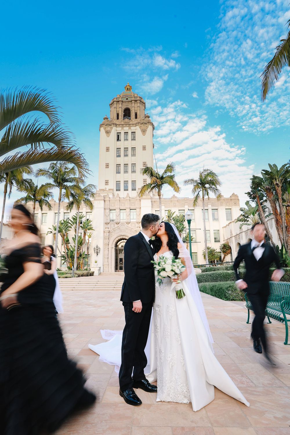 Elegant wedding couple dances with blurred motion on a grand palm-lined plaza in front of historic Beverly hills city hall