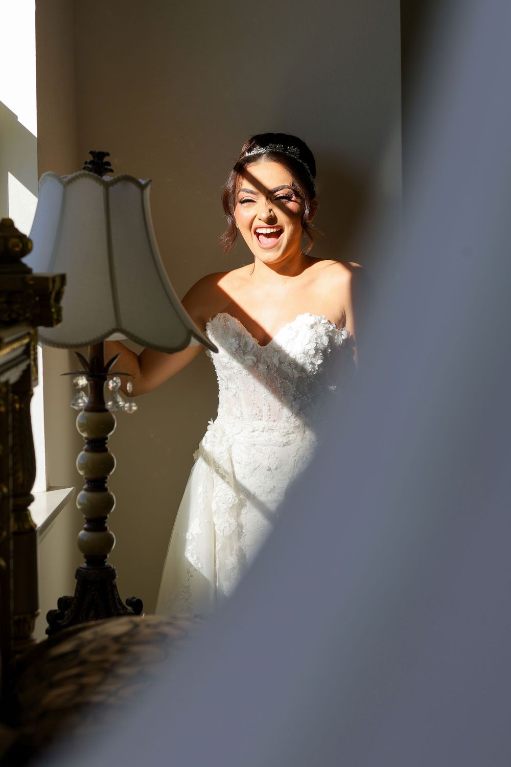 A bride in a white lace wedding dress poses in dramatic window lighting creating beautiful shadows and highlights.
