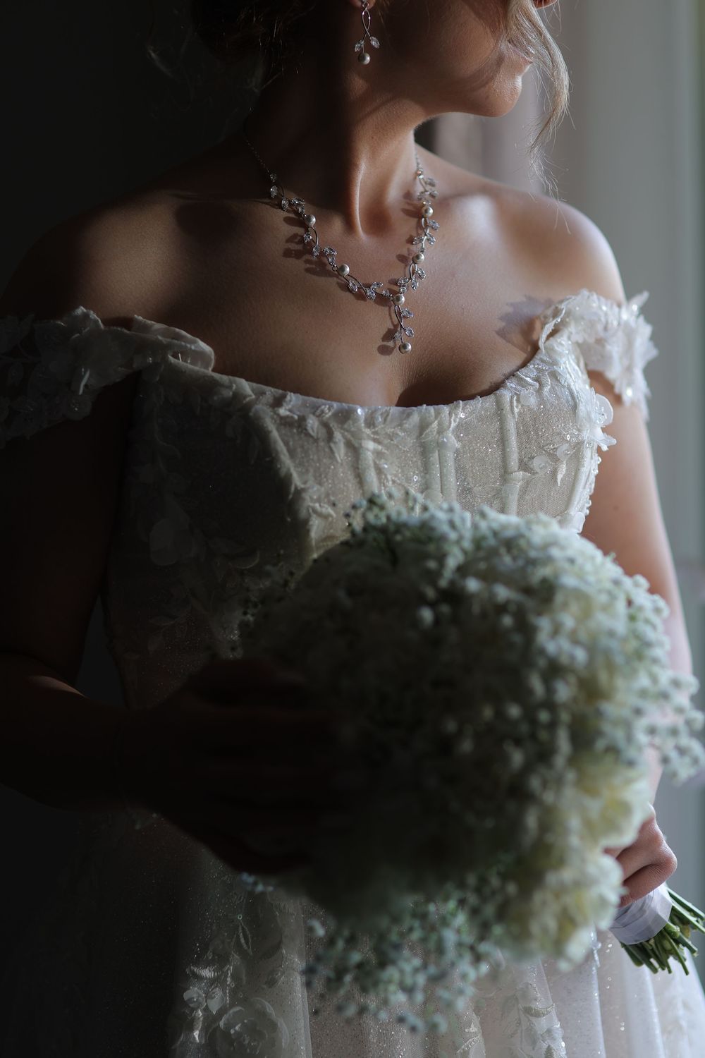 Close-up detail of a wedding dress bodice with delicate lace trim and a sparkling crystal necklace.