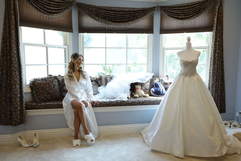 A bridal preparation scene with an elegant wedding gown displayed by a window seat and brown curtains draping above.
