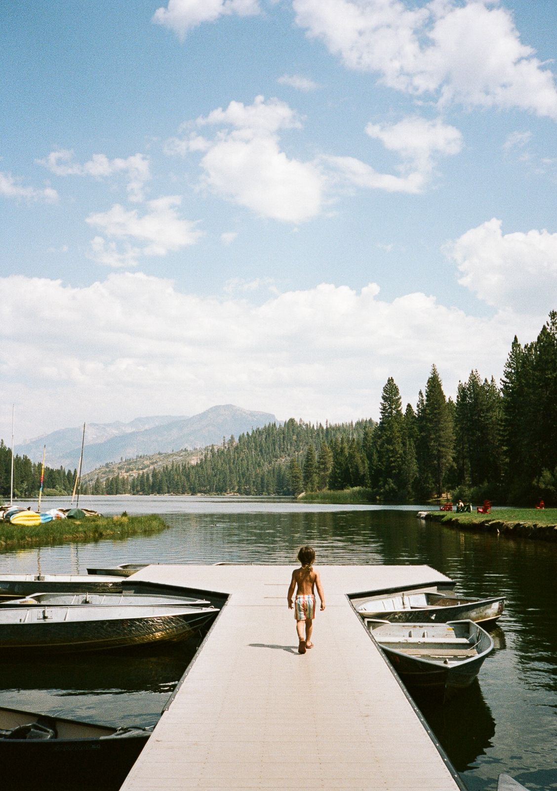 Walking down a dock lined with boats on a mountain lake surrounded by pine forests.