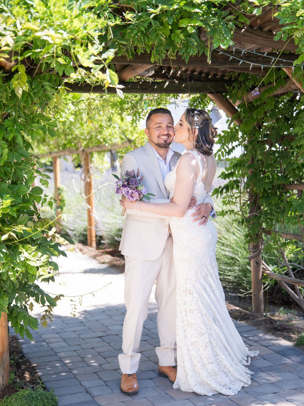 Newlyweds share a romantic moment under a lush garden arbor decorated with greenery and flowers.