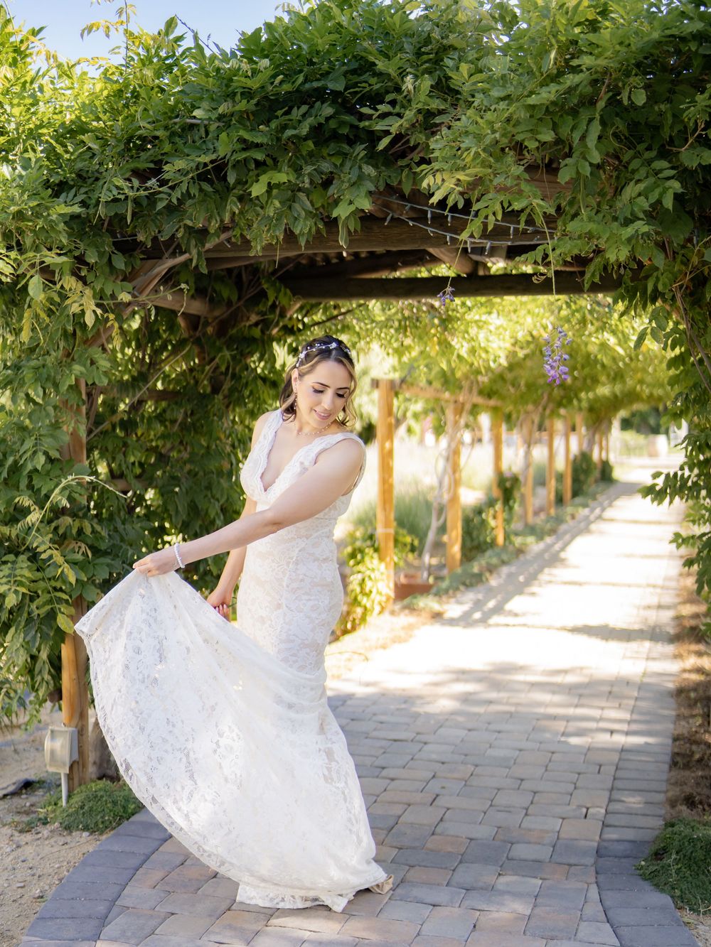 A person in a white wedding dress spins gracefully along a stone garden pathway surrounded by lush green foliage.