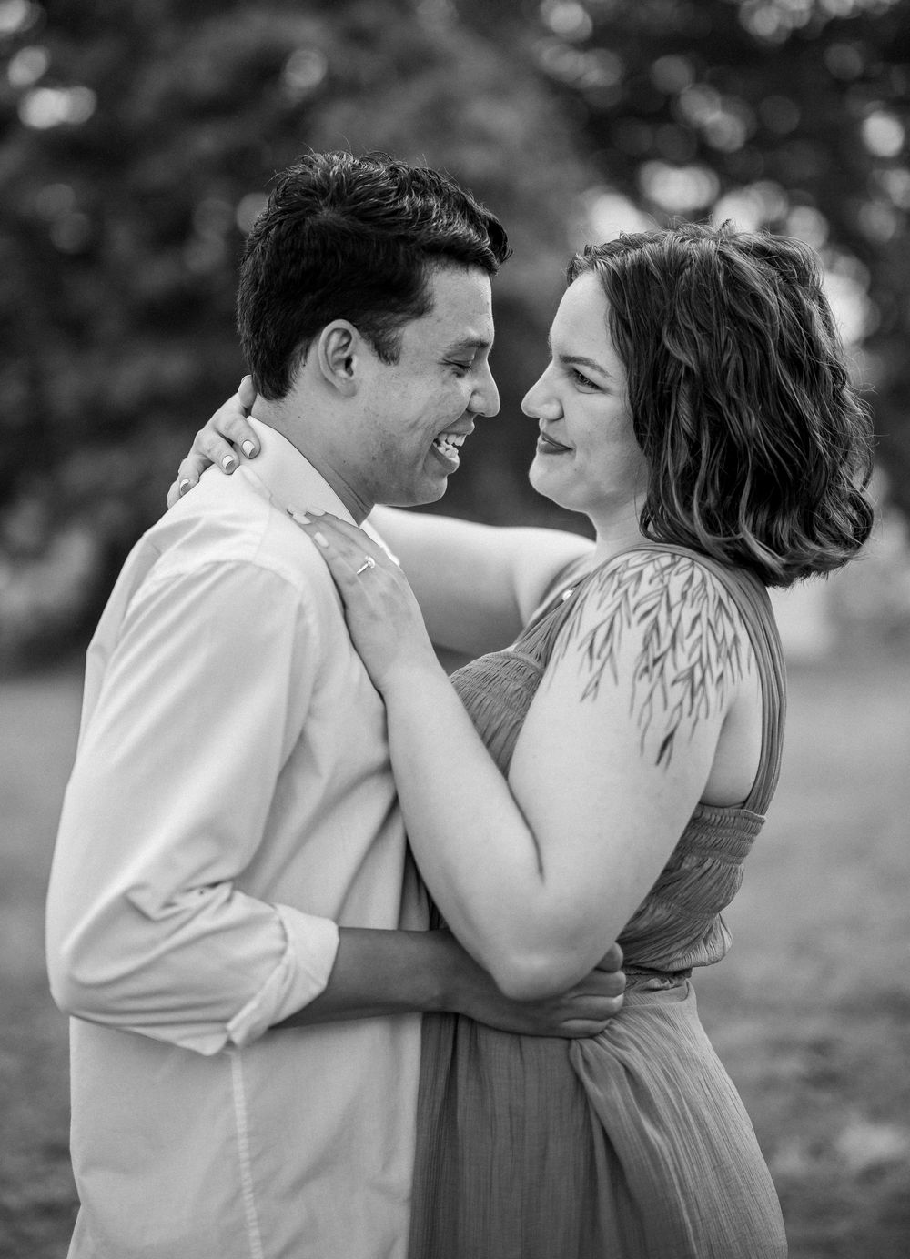Black and white portrait of a couple embracing and laughing together outdoors in a tender romantic moment.