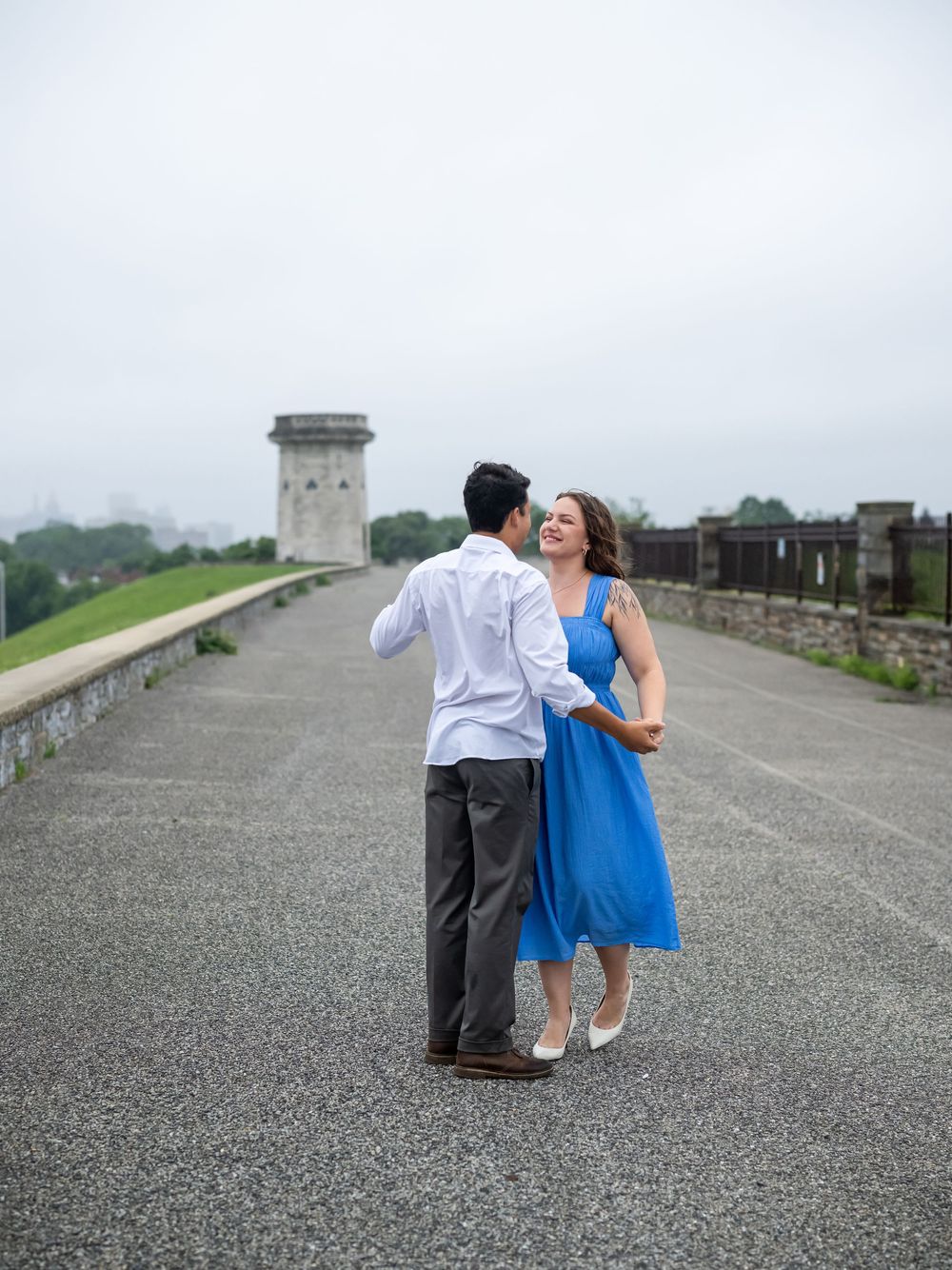 A couple dancing and laughing together on a stone pathway with a foggy fortress wall and tower in the background, in baltimore