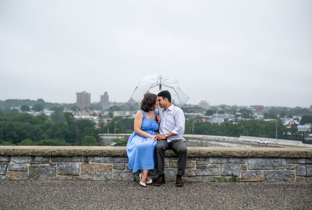 A couple shares a romantic moment together on a stone wall overlooking a misty cityscape in Baltimore