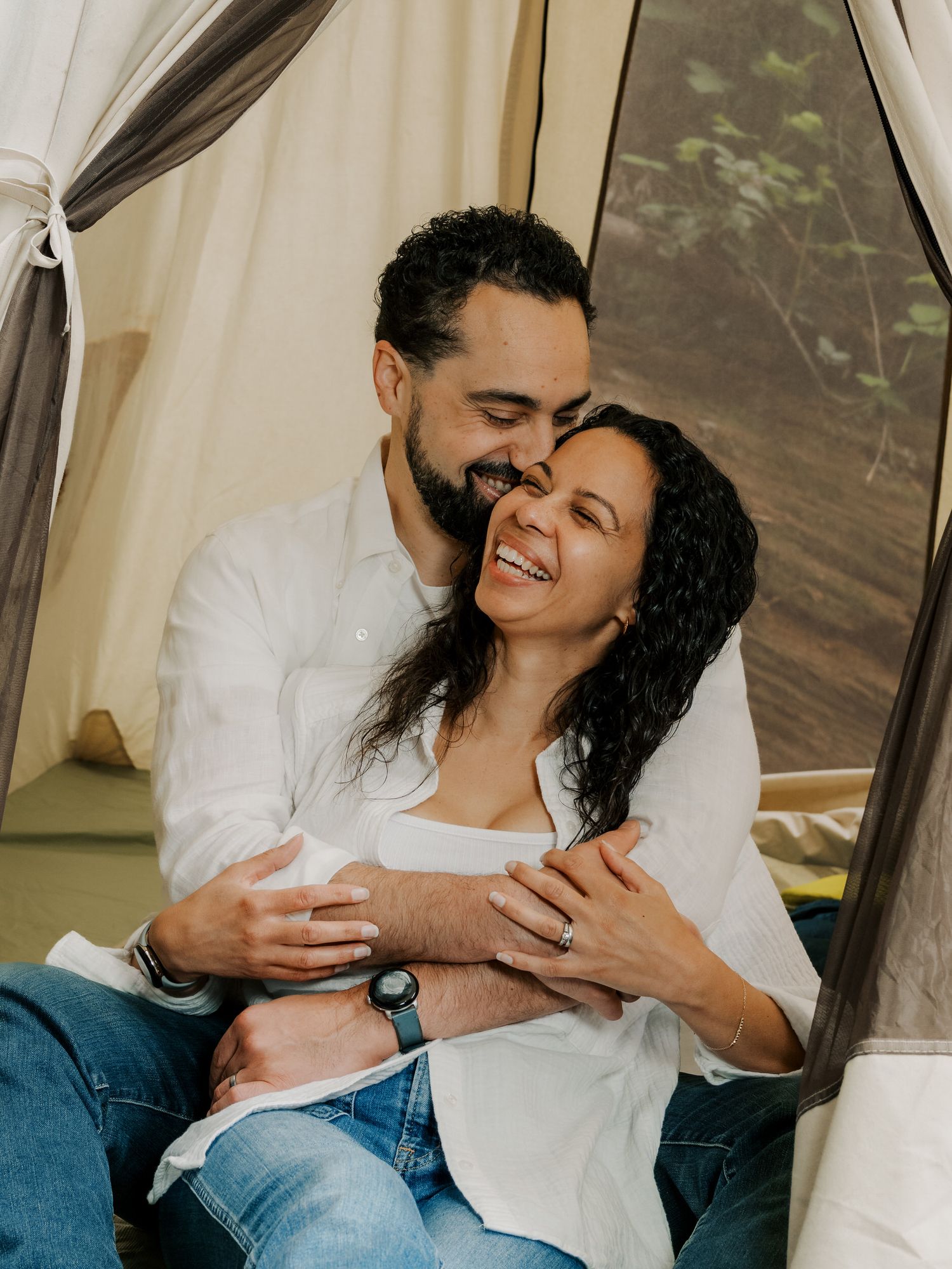 Affectionate couple sharing an intimate, joyful moment together while relaxing in a tent with natural light.