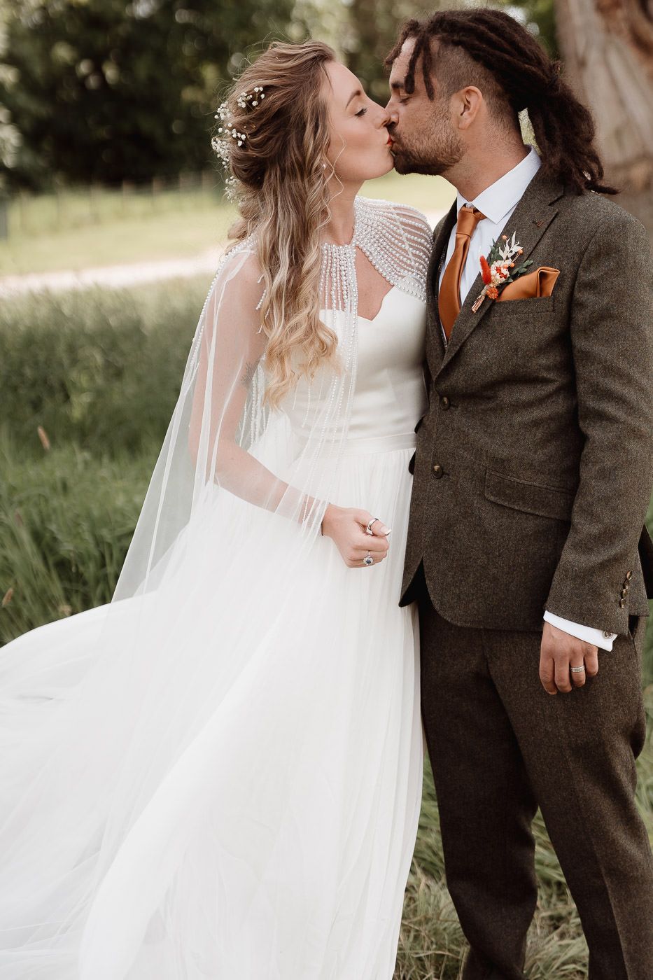 Romantic wedding couple embraces in long white dress and brown suit outdoors with soft natural lighting.