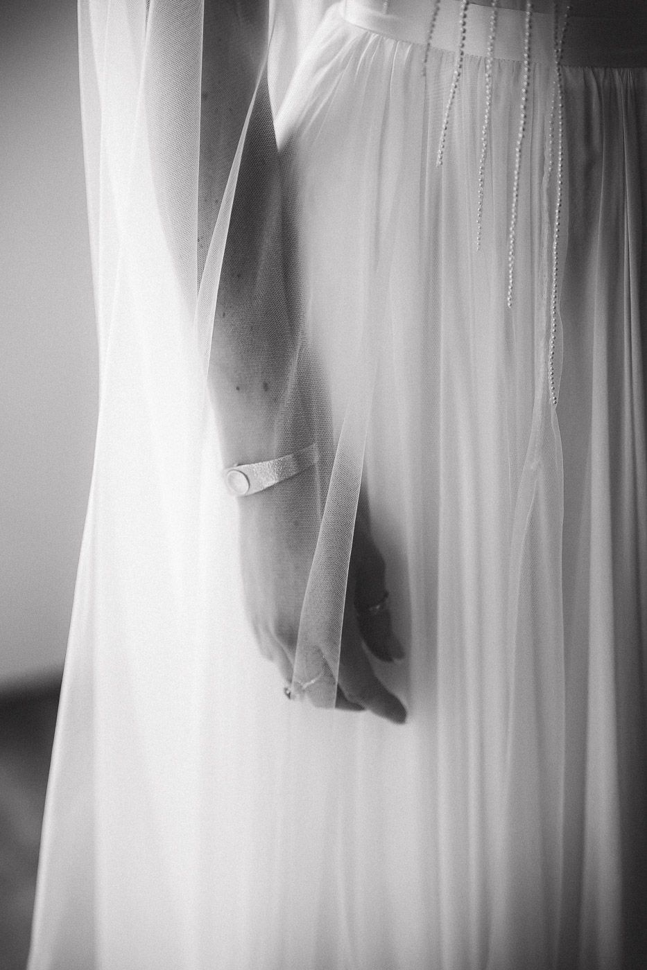 Black and white image of flowing bridal wedding gowns displayed on hangers in an elegant setting.