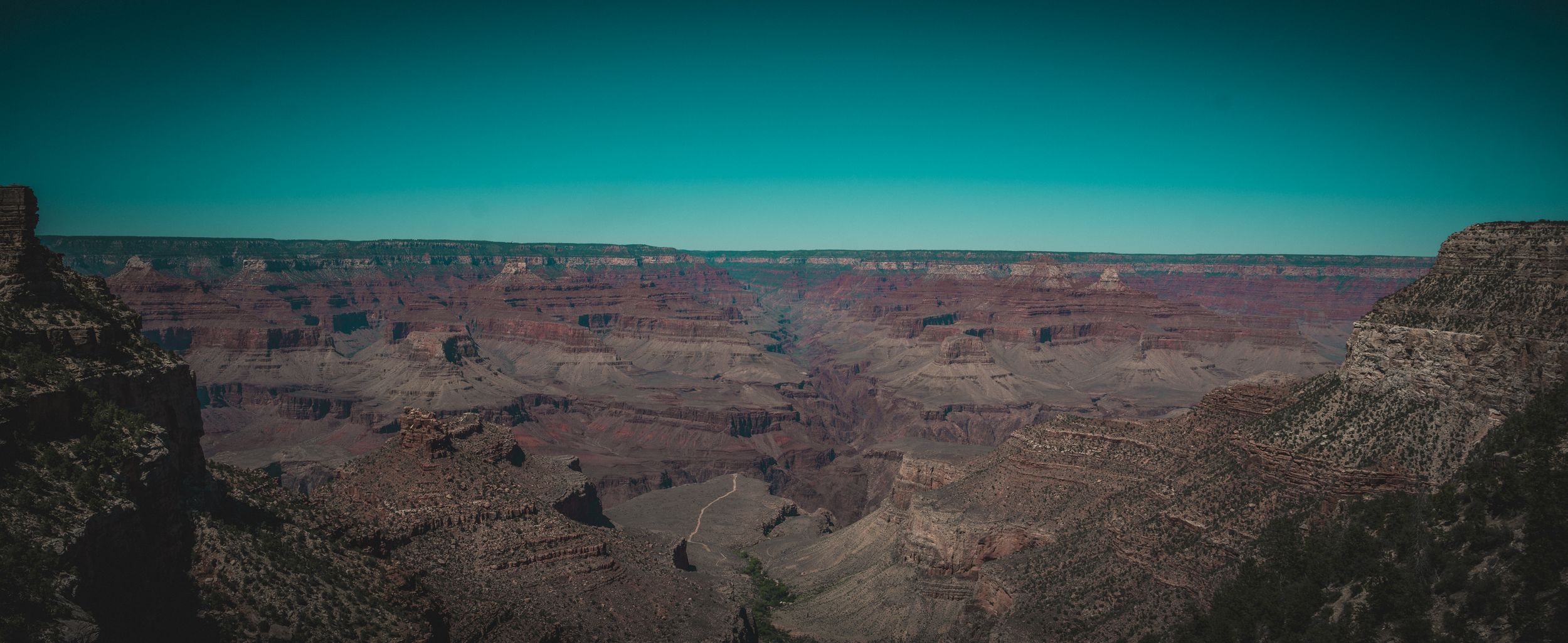 Sweeping panoramic view of the Grand Canyon landscape under turquoise sky.