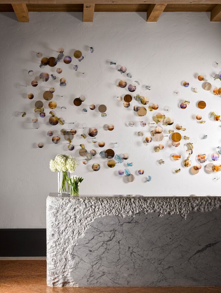 Modern interior design featuring a textured stone counter with white flowers against a wall adorned with floating metallic discs.