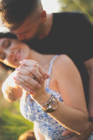 two hands intertwined with an engagment ring in the foreground the couple heads close togther in the background