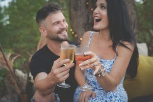 Engagement photography showing a awestruck lady holding a glass  of champagne with her ring in the foreground and smiling fiance in back