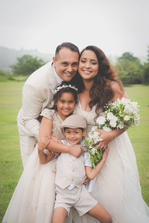 A wedding photo of the bride and groom with their younger children all looking at the camera in a family embrace