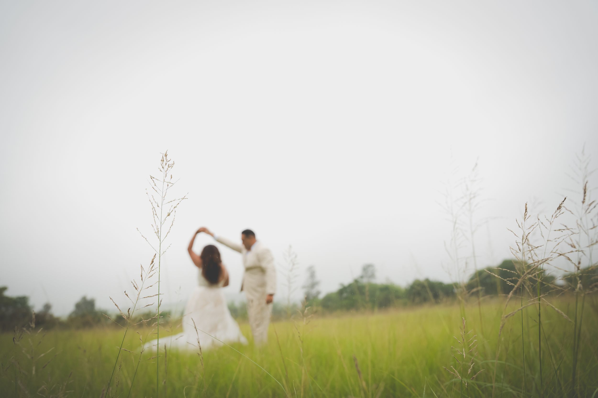 A field where a groom holds his brides hand as he swirls her in a dance move