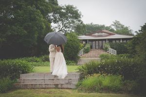 A bride and groom kissing in an outdoor scene with the faces hidden by and umbrella