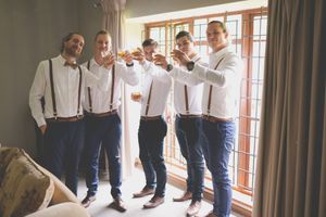 A grooms party toast their whisky glasses toward the camera all dressing in the wedding atire.