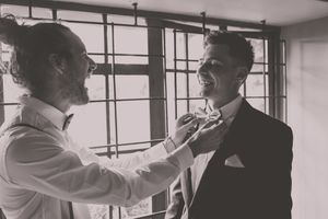 A groom and groomsman fixing the grooms bowtie as they laugh together