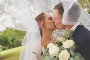A bride and groom kissing under the brides veil and the wedding boquet or white roses in the foreground