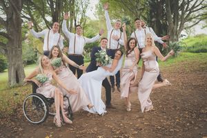 A wedding party in a fun jumping pose together while groom dips the bride in a dance move and everyone happy in an outdoor scene