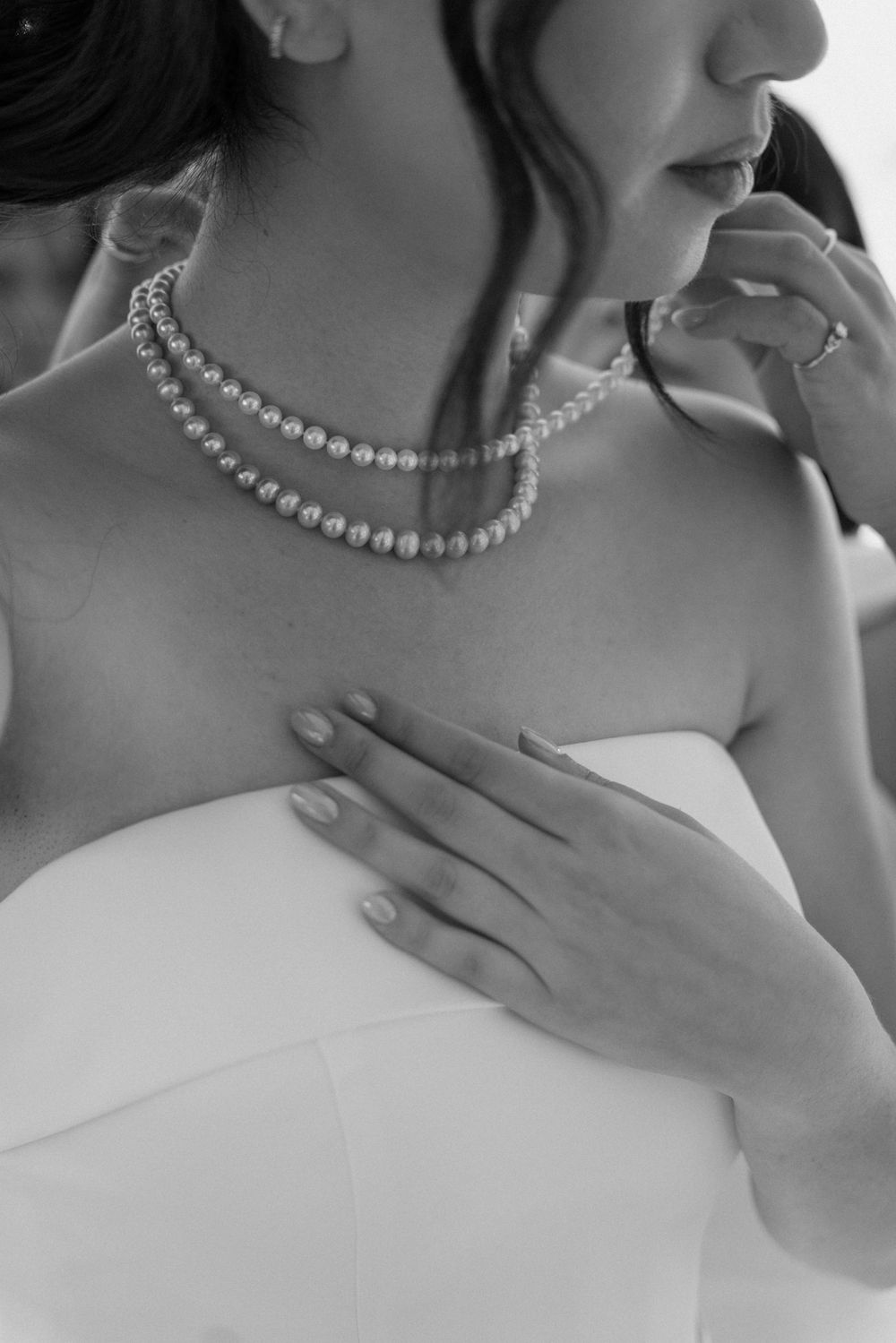 Close-up black and white photo of a bride wearing a double strand pearl necklace in a white gown.