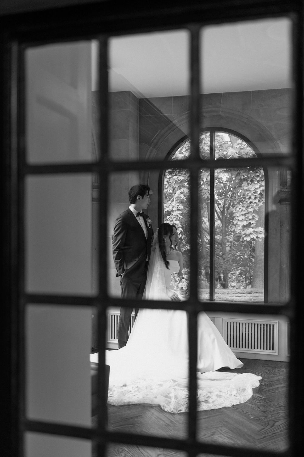Artistic black and white shot of bride and groom framed through window panes in elegant venue.