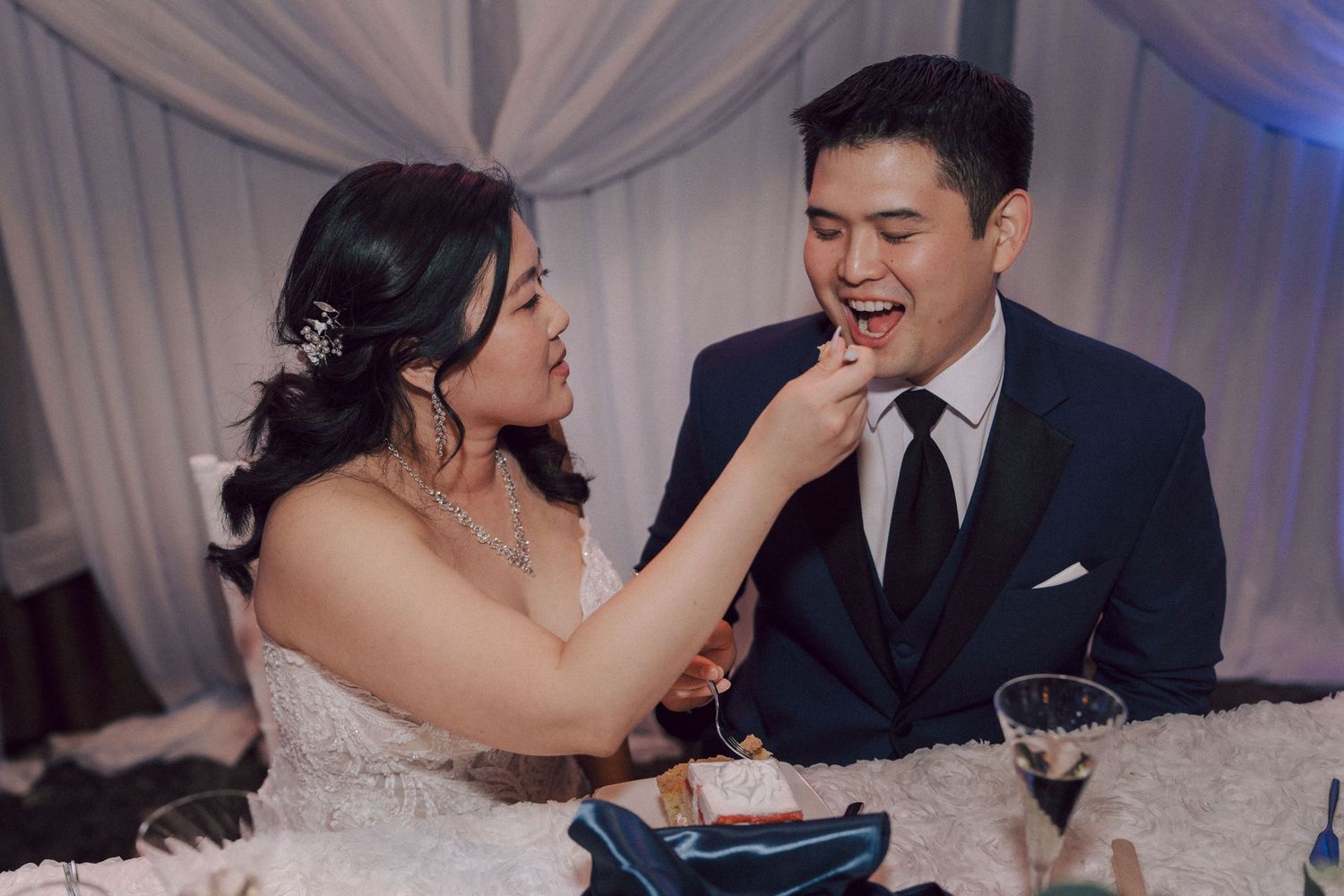 A sequence of wedding cake feeding moments between newlyweds in formal attire under white draping decor.